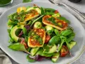 Kolorowa sałatka z grillowanym halloumi, awokado, pomidorkami i ogórkiem, polana zielonym sosem.