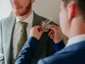 Un homme ajuste une boutonnière sur le costume d'un autre. Divers types de boutonnières existent, celle-ci est composée de fleurs séchées et de feuillages dorés.