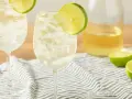 Orzeźwiający szprycer co to? Dwa kieliszki białego wina z lodem i plasterkiem limonki, obok butelka wina i połówki limonki.