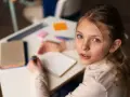 Dziewczynka zmagająca się z dysleksją rozwojową próbuje pisać w zeszycie, patrząc z nadzieją na pomoc.