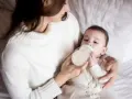 Mama karmi butelką dziecko, które właśnie pije mleko. Ważne jest, ile mleka powinien jeść noworodek.