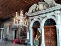 Una donna in un abito verde posa davanti a un portale decorato in una casa museo a Venezia, con un lampadario di cristallo e dipinti alle pareti.