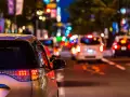 Luci sfocate e colorate in una strada trafficata di notte, come vedono i miopi le luci. Un'auto argentata in primo piano.