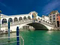 Ponte di Rialto, un'icona della storia veneziana, con le sue botteghe e la folla che lo attraversa, si specchia nelle acque verdi del Canal Grande.