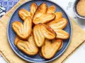 Un piatto blu pieno di dolci con pasta sfoglia dorati e croccanti, cosparsi di zucchero.
