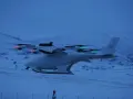 A white vtol drone with red and green lights flies over a snowy landscape at dusk.