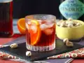 Przepis na Negroni Sbagliato: orzeźwiający drink z pomarańczą i lodem, obok miseczka pistacji.