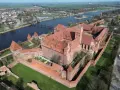 Potężny zamek z czerwonej cegły, największy zamek w Europie, otoczony murami obronnymi, nad rzeką.