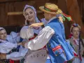 Uśmiechnięta para w tradycyjnych strojach tańczy do skocznych piosenek ludowych.