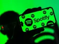 Dłoń trzyma smartfon z zielonym ekranem, na którym widnieje logo Spotify. Użytkownik cieszy się doskonałą spotify jakość dźwięku.