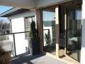 Nowoczesny balkon z drewnianymi, podwójnymi drzwiami balkonowymi. Okna dzielone poziomo wpuszczają dużo światła.
