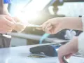Dwie dłonie przekazują sobie pieniądze. Obok terminal płatniczy i karty. Klientka dokonuje zwrot bez paragonu.