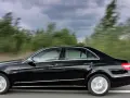 Czarny Mercedes E350 pędzi po drodze, mijając rozmyte zielone drzewa.