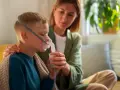 Chłopiec z maską nebulizatora, wspierany przez matkę. Dbałość o zdrowie dziecka z astmą wczesnodziecięcą.