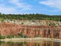 En sjö speglar Sveriges Grand Canyon, en imponerande klippformation med lager av röd och grå sten, krönt av en grönskande skog.
