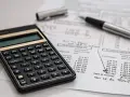 Calculadora y bolígrafo sobre un balance de situación. El balance de situación muestra cifras de inversión y valor al cierre del año.