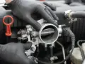 Mechanik w czarnych rękawiczkach sprawdza przepustnicę. Objawy uszkodzonego czujnika położenia przepustnicy mogą być różne.