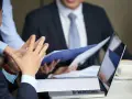 Personas discuten documentos y gráficos, quizás sobre la demora de calificación de incapacidad permanente.