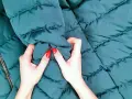 Manos con uñas rojas arrugan una chaqueta verde oscuro. ¡Por fin he lavado un plumas en la lavadora y está como nuevo!