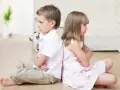 Dzieci siedzą plecami do siebie, obrażone. Czy to przez bycie gorszym dzieckiem? Kotek w tle.
