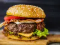 Hamburger di carne succulento con bacon croccante, formaggio fuso, pomodoro e lattuga su panino ai semi di sesamo.