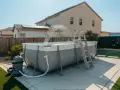 Above ground pool installation in progress, with water spraying from the filter system. A ladder is attached, ready for summer fun.