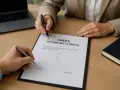 Podpisanie aneksu do umowy o pracę. Dwie osoby przy biurku z dokumentem i długopisami.