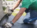 Trabajador realiza impermeabilización de terrazas, cortando material para asegurar la protección contra el agua.