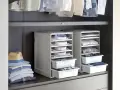 Organizzazione armadio: camicie piegate in contenitori modulari, pile di vestiti e un cappello su una mensola.