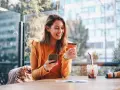 Smiling woman uses phone and credit card. She's researching if you need an LLC for a business credit card.