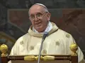 Uśmiechnięty prezbiter w złotej szacie z ozdobnymi haftami przemawia do mikrofonu.