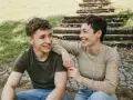 Ein lachendes Mutter-Sohn-Gespann sitzt im Freien vor einer Steintreppe.