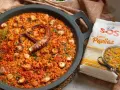 Paella de marisco con un tentáculo de pulpo visible, gambas y trozos de calamar. Al lado, un paquete de arroz SOS Especial Paellas.
