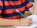 Chłopiec w pasiastej koszulce zmaga się z pisaniem, trzymając ołówek.