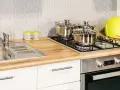 Nowoczesna kuchnia z drewnianym blatem, na którym stoi zlew, kuchenka z garnkami i żółty chlebak. Szerokość blatu kuchennego pozwala na wygodne gotowanie.