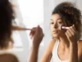 Une jeune femme applique du fond de teint avec un pinceau. Elle se demande combien de temps garder une palette de maquillage pour une peau parfaite.
