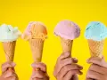 Vier Hände halten bunte Speiseeiswaffeln vor gelbem Hintergrund. Die ideale Temperatur für Speiseeis.