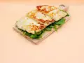 Trzy złociste plastry sera halloumi na desce z rukolą. Czy w ciąży można jeść ser halloumi? Tak, jeśli jest pasteryzowany.