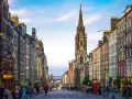 Edinburgh's Royal Mile with a clock tower and people walking on a cobblestone street.