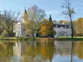 Pałac w jesiennej scenerii nad jeziorem, część Bolimowskiego Parku Krajobrazowego. Kaczka pływa po wodzie.