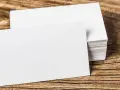 Pila de tarjetas de visita blancas sobre madera. Se aprecian los diferentes grosores de papel en la pila.