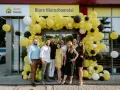 Grupa ludzi pozuje przed biurem nieruchomości ozdobionym żółtymi balonami.