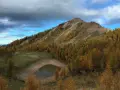 Autunno dorato sul lago delle salare, con larici color ocra che abbracciano la montagna e riflettono il cielo nuvoloso.