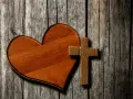 Holzherz und Kreuz auf grober Holzoberfläche. Ein Symbol für Liebe und Glauben, wie in Lukas 23,34.
