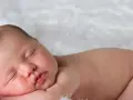 Śpiące, 3 miesięczne dziecko z delikatnymi włoskami, wtulone w miękkie futerko.