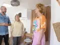 Trzy osoby omawiają remont przyczepy kempingowej. Wnętrze jest jasne, z widocznym łóżkiem i meblami.
