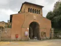 The imposing facade of Tre Fontane Abbey, with its arched entrance and upper loggia, stands against a cloudy sky.