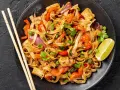 Pyszny pad thai z kurczakiem, warzywami i makaronem ryżowym, udekorowany kolendrą i ćwiartką limonki.