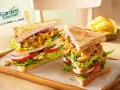 Zwei üppige Garden Gourmet Club Sandwiches mit knackigem Salat, Tomaten, Gurken und Zwiebeln auf getoastetem Brot.