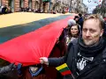 Ludzie niosą ogromną flagę Litwy podczas święta narodowego. Na twarzach uczestników widać patriotyczne barwy.